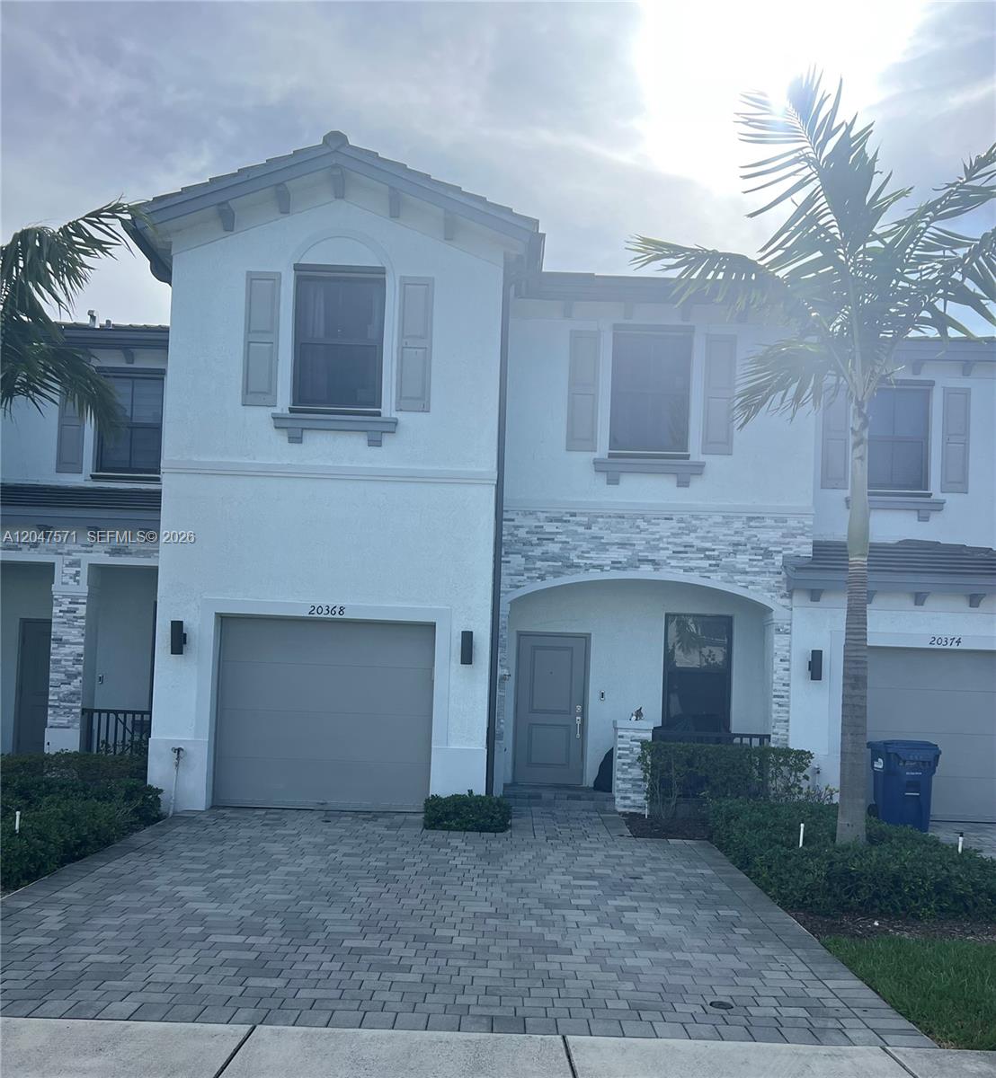A two-story townhouse features a gray garage door, stone accents, and a paved driveway — 20368 NW 4th Path, Miami Gardens FL 33169, MIAMI GARDENS, FL