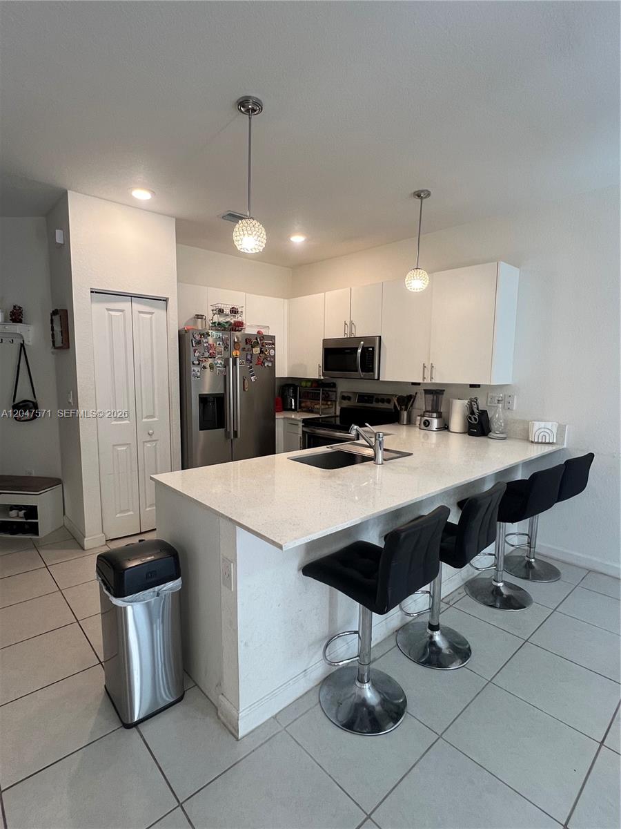 A kitchen features white cabinets, stainless steel appliances, a quartz island, and three bar stools — 20368 NW 4th Path, Miami Gardens FL 33169, MIAMI GARDENS, FL