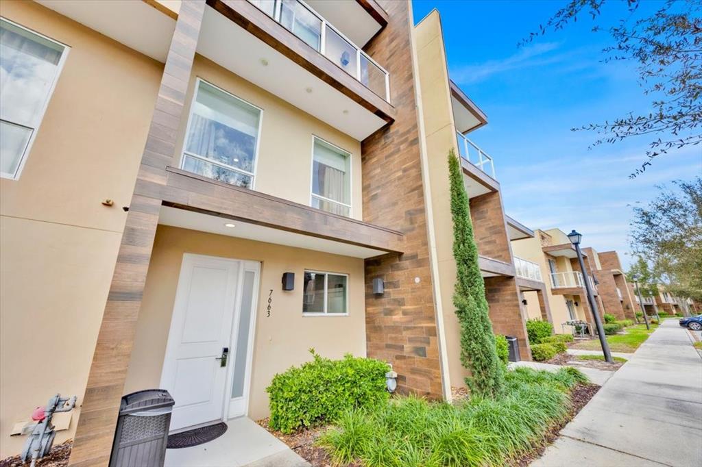 A modern three-story townhouse exterior features tan stucco, wood-look siding, and a white front door — 7663 RECIFE DRIVE, KISSIMMEE, FL