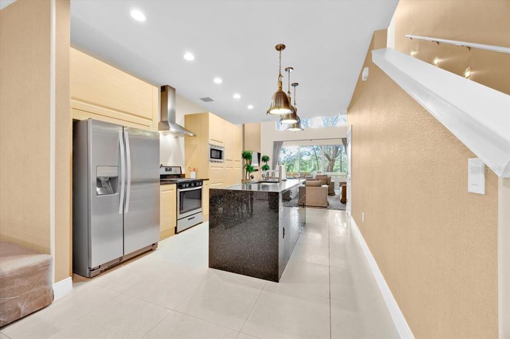 A modern kitchen features stainless steel appliances, a dark granite island, and light-colored tile flooring — 7663 RECIFE DRIVE, KISSIMMEE, FL