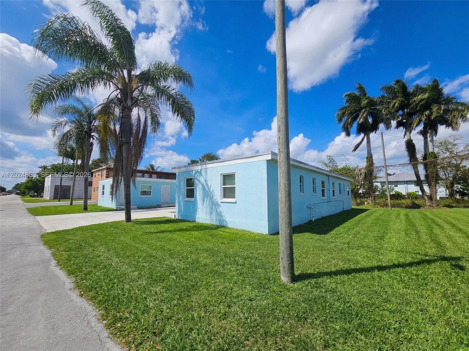 A light blue single-story building sits on a grassy lot with several palm trees — 625 W Avenue A, Belle Glade FL 33430, BELLE GLADE, FL