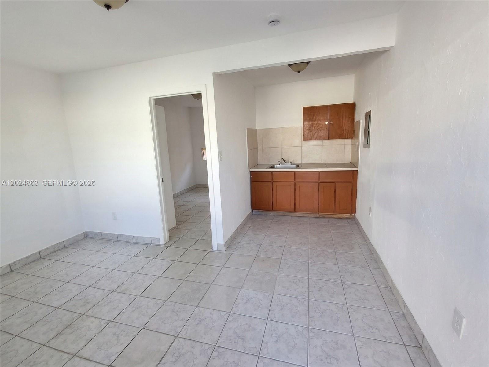 A small kitchen area with wooden cabinets and tiled floors leads into an adjacent room — 625 W Avenue A, Belle Glade FL 33430, BELLE GLADE, FL