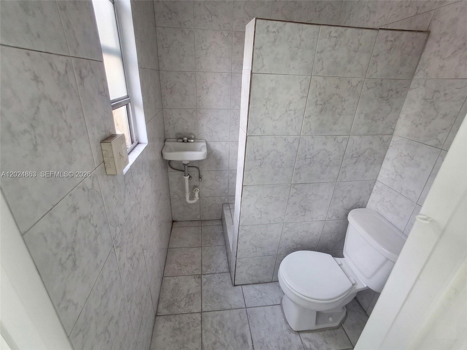 A small bathroom features light gray marble-patterned wall tiles, a pedestal sink, and a toilet — 625 W Avenue A, Belle Glade FL 33430, BELLE GLADE, FL