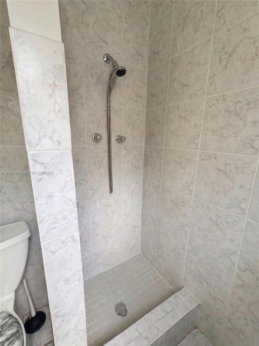 A tiled walk-in shower features a handheld showerhead and a small curb — 625 W Avenue A, Belle Glade FL 33430, BELLE GLADE, FL