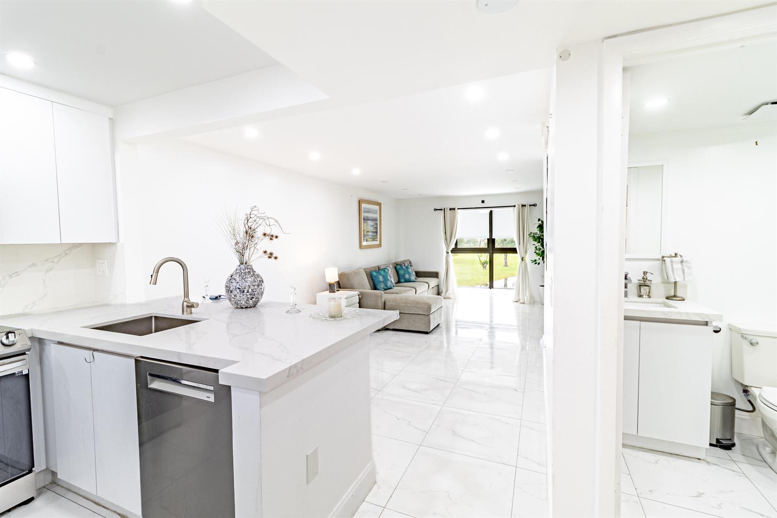 A modern kitchen with white cabinets and marble countertops opens into a bright living area — 10331 Sunrise Lakes Boulevard # 302, Sunrise FL 33322, SUNRISE, FL