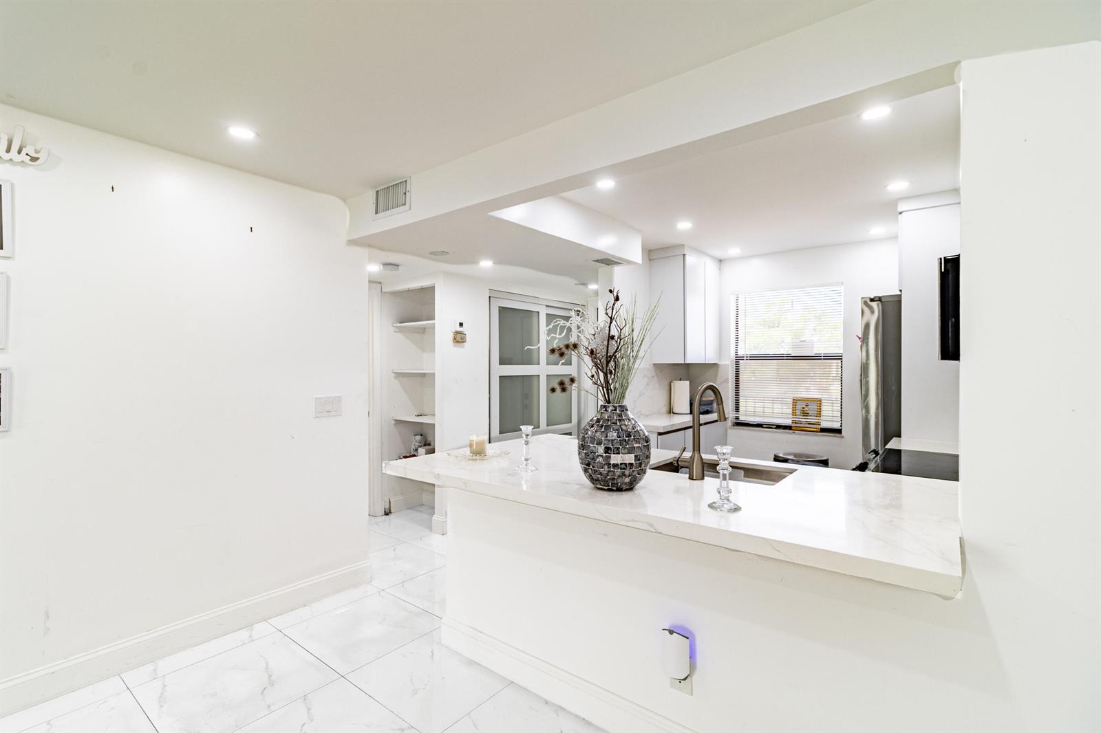 A bright kitchen features white cabinets, a marble-topped breakfast bar, and white tiled flooring — 10331 Sunrise Lakes Boulevard # 302, Sunrise FL 33322, SUNRISE, FL