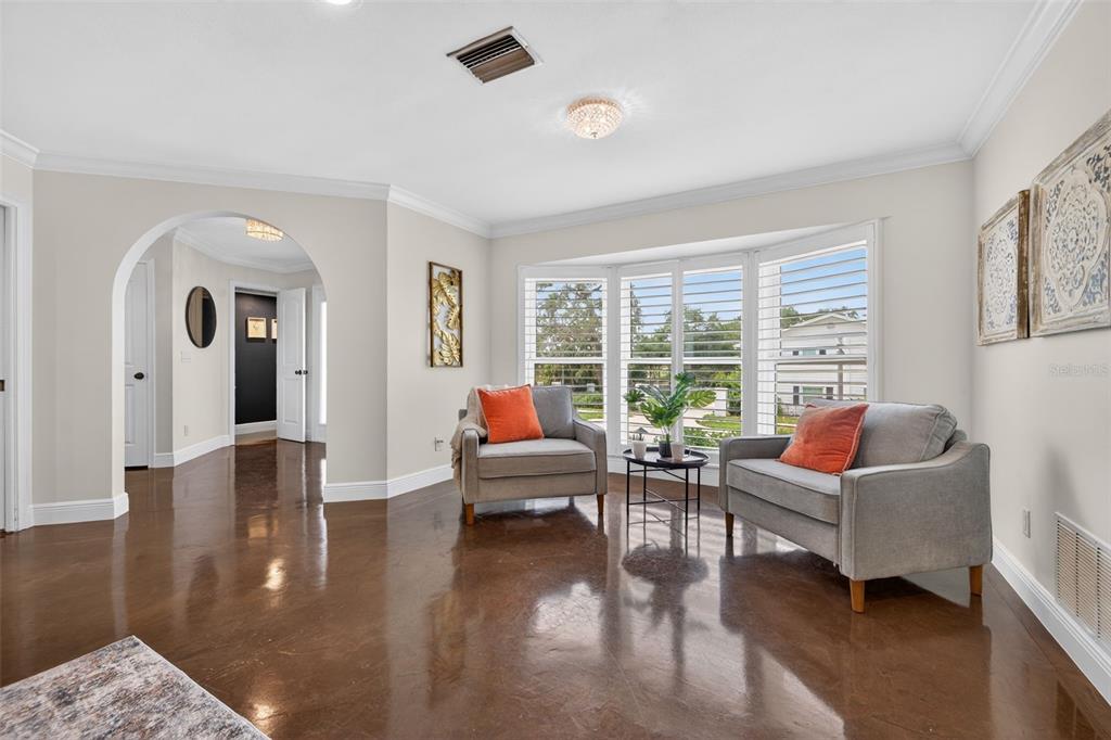 A living room with polished concrete floors, two gray armchairs, and a large bay window — 303 ROEBLING ROAD S, BELLEAIR, FL