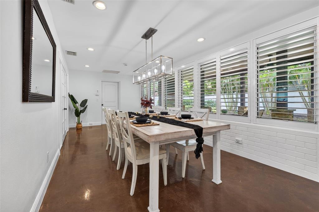 A dining room features a long wooden table, white chairs, and plantation shutters on windows — 303 ROEBLING ROAD S, BELLEAIR, FL