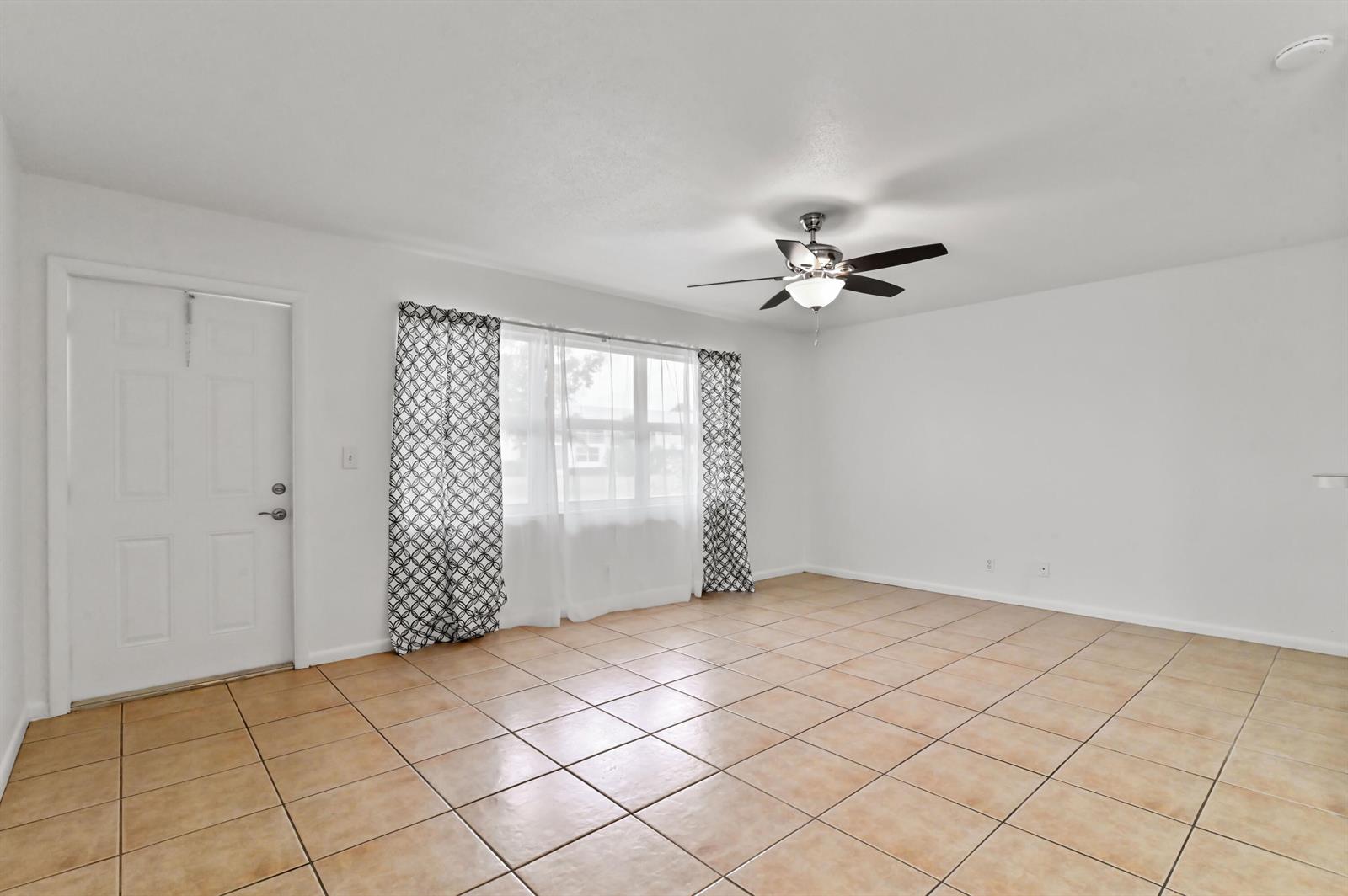 An empty living room features white walls, tan tile flooring, and a ceiling fan — 149 Coventry # G, West Palm Beach FL 33417, WEST PALM BEACH, FL