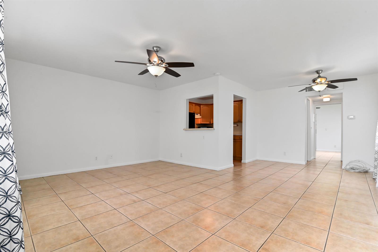 An open living area features white walls, tan tile flooring, and two ceiling fans — 149 Coventry # G, West Palm Beach FL 33417, WEST PALM BEACH, FL