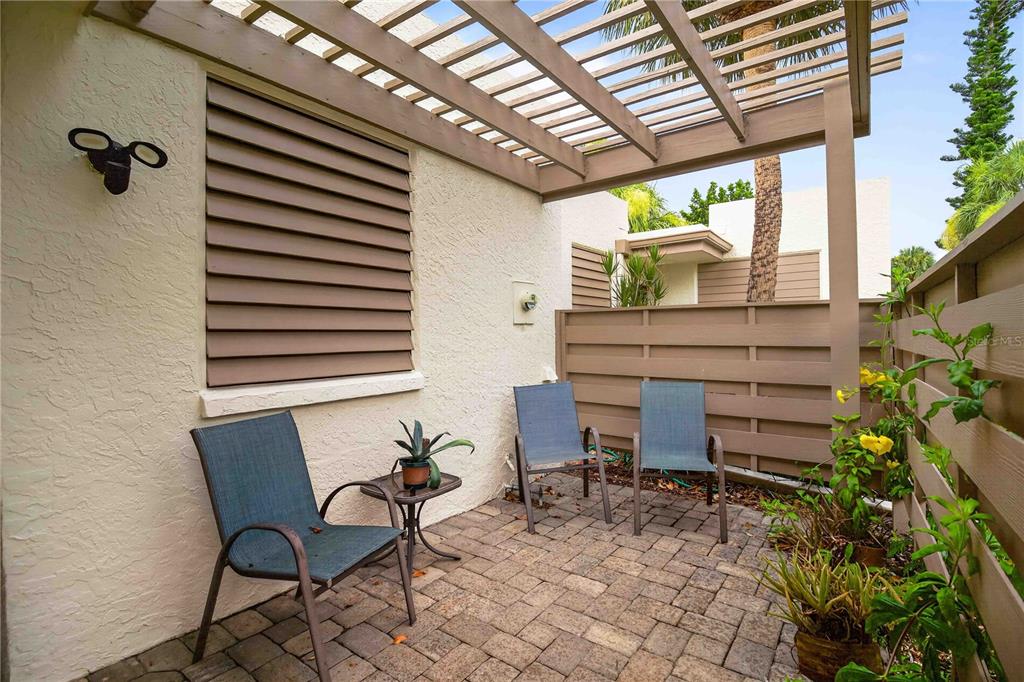 A small patio features a wooden pergola, brick pavers, three chairs, and a privacy fence — 755 OAKVIEW DRIVE, BRADENTON, FL
