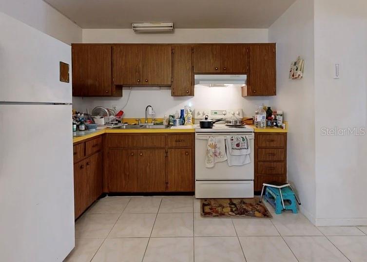 A kitchen with wood cabinets, yellow countertops, white appliances, and light-colored tile flooring — 2336 JAVA PLUM AVENUE, SARASOTA, FL