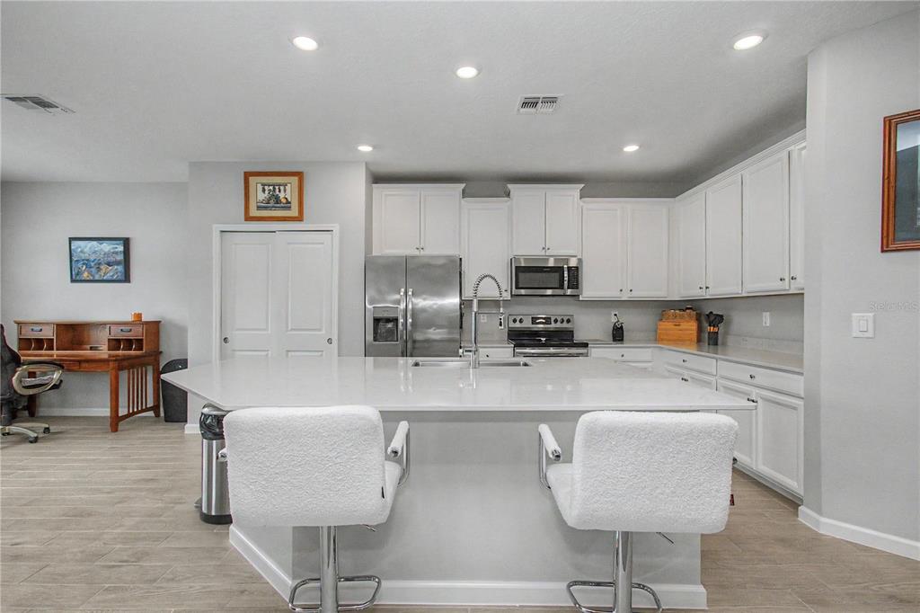 A kitchen features a large white island, stainless steel appliances, and white cabinetry — 7369 SW 77TH AVENUE, OCALA, FL