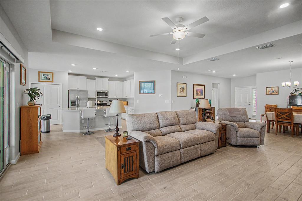 An open-concept living room and kitchen feature light tile flooring, white cabinetry, and neutral furniture — 7369 SW 77TH AVENUE, OCALA, FL