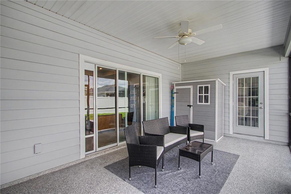A covered patio features gray siding, a ceiling fan, outdoor furniture, and a small storage shed — 7369 SW 77TH AVENUE, OCALA, FL