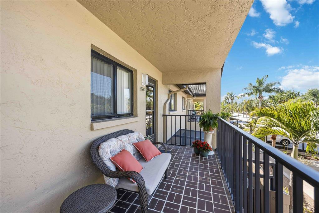 A covered balcony features a wicker loveseat, tiled flooring, and a black metal railing — 5515 ASHTON WAY UNIT 5515, SARASOTA, FL