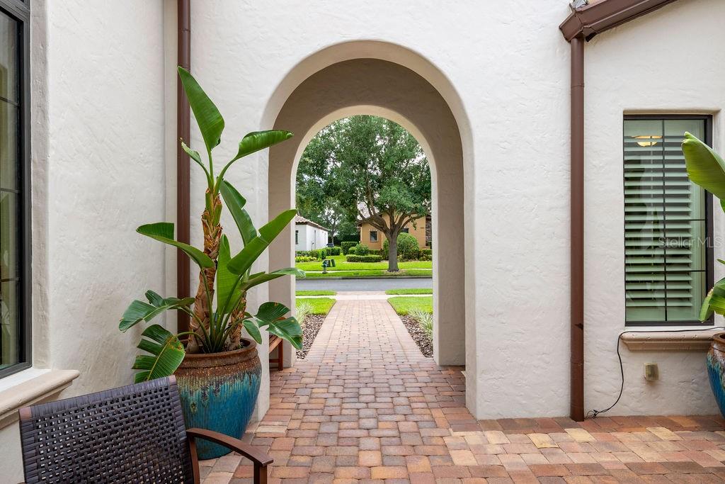 An arched entryway leads from a paved courtyard to a street with trees and houses — 11832 WATERSTONE LOOP DRIVE, WINDERMERE, FL