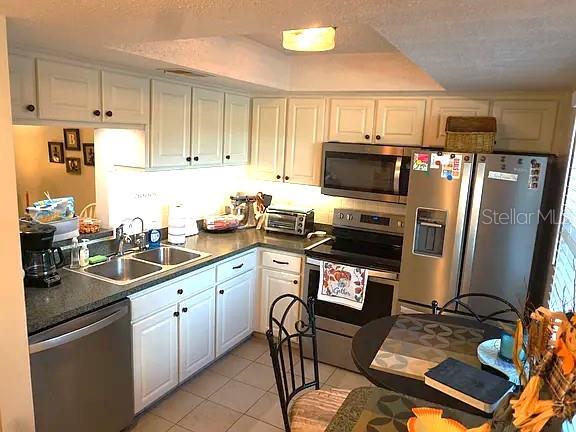 A kitchen features white cabinets, stainless steel appliances, and a small dining table — 841 PATRICIA AVENUE UNIT 206, DUNEDIN, FL