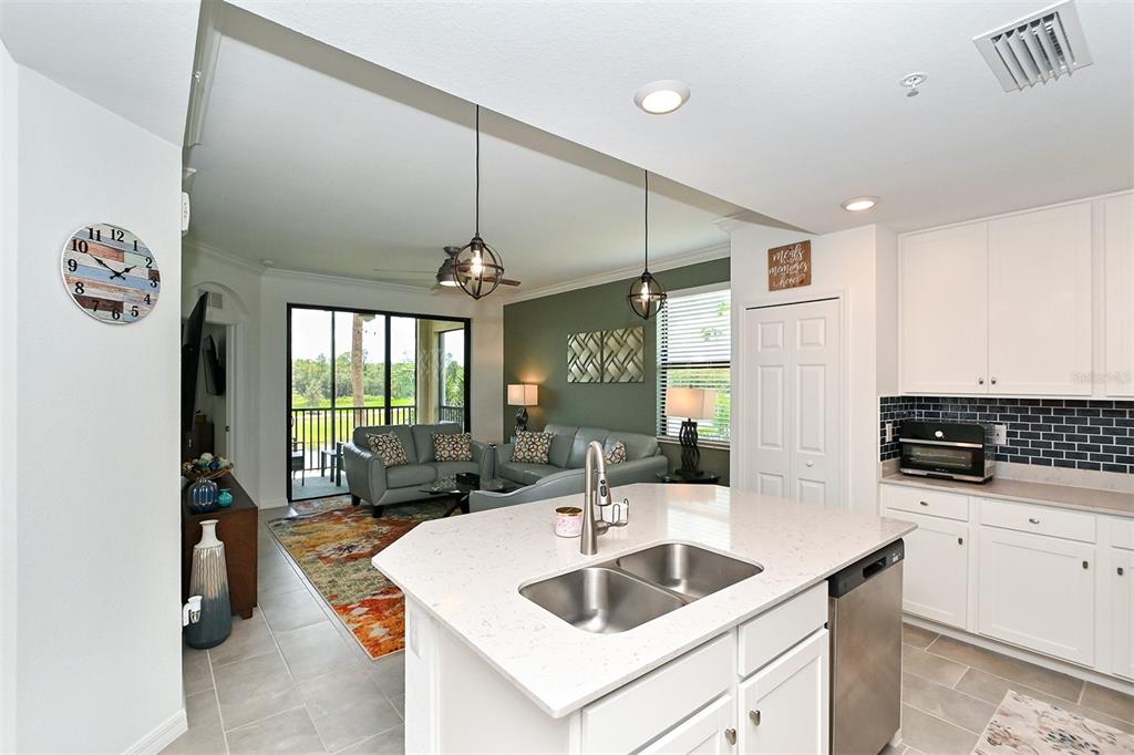 A kitchen with a white island and quartz countertops overlooks a living room with green walls — 18028 GAWTHROP UNIT 208, LAKEWOOD RANCH, FL