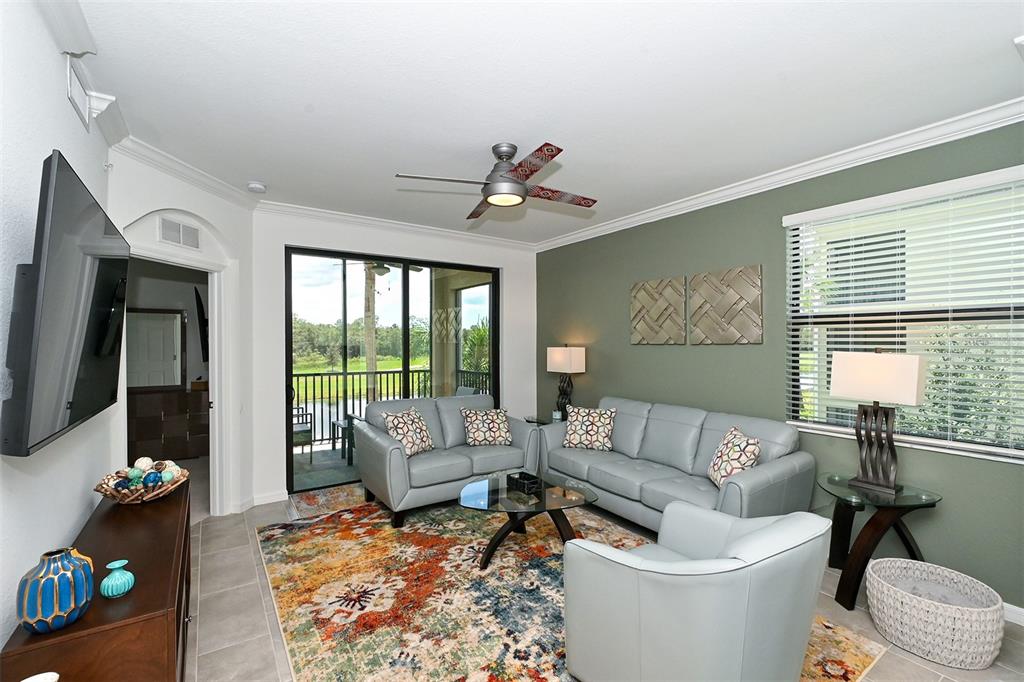 A living room features light blue leather furniture, a colorful area rug, and a green wall — 18028 GAWTHROP UNIT 208, LAKEWOOD RANCH, FL