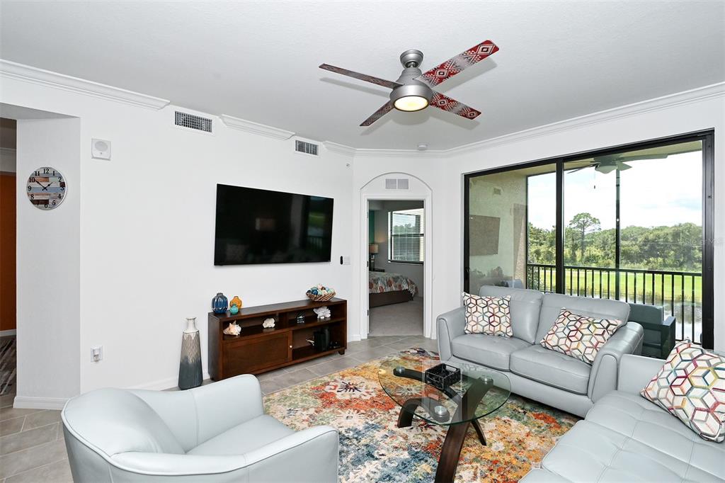 A living room features a television, a ceiling fan, light-colored sofas, and a patterned rug — 18028 GAWTHROP UNIT 208, LAKEWOOD RANCH, FL