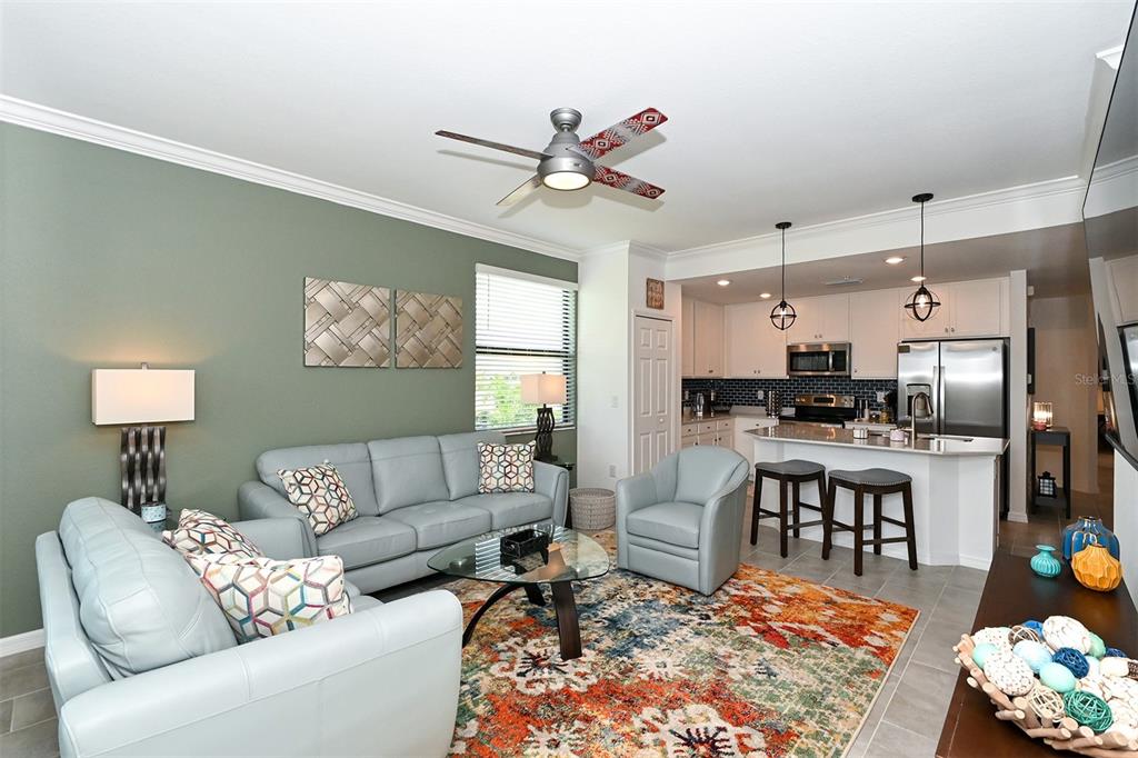 A living room with light blue furniture, a colorful area rug, and an open kitchen — 18028 GAWTHROP UNIT 208, LAKEWOOD RANCH, FL