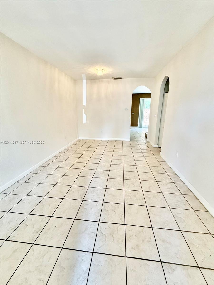 An empty room features light-colored tile flooring, white walls, and an arched doorway — 5770 NW 113th Pl, Doral FL 33178, DORAL, FL