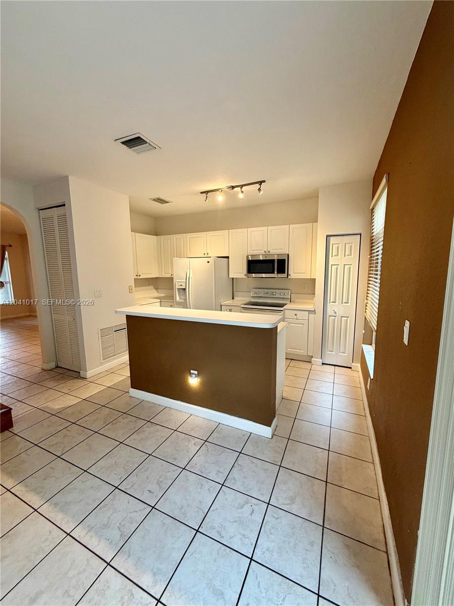 A kitchen features white cabinets, a brown breakfast bar, and light-colored tile flooring — 5770 NW 113th Pl, Doral FL 33178, DORAL, FL