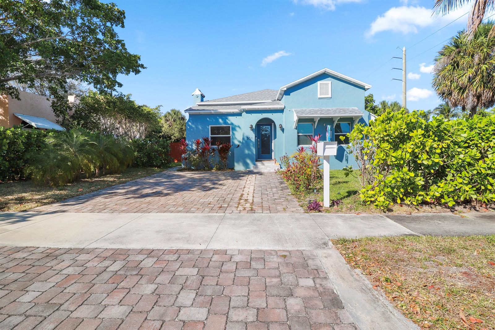 A blue single-story house features a brick driveway and a front yard with landscaping — 301 Hawthorne Drive, Lake Park FL 33403, LAKE PARK, FL