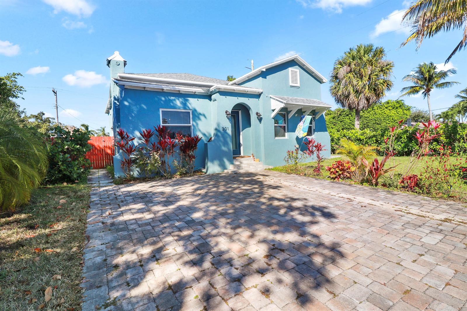 A blue single-story house with a paved driveway and tropical landscaping under a blue sky — 301 Hawthorne Drive, Lake Park FL 33403, LAKE PARK, FL
