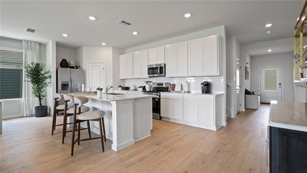 A modern kitchen features white cabinetry, a central island with bar stools, and light wood flooring — 1880 FIELDSTONE STREET, MINNEOLA, FL