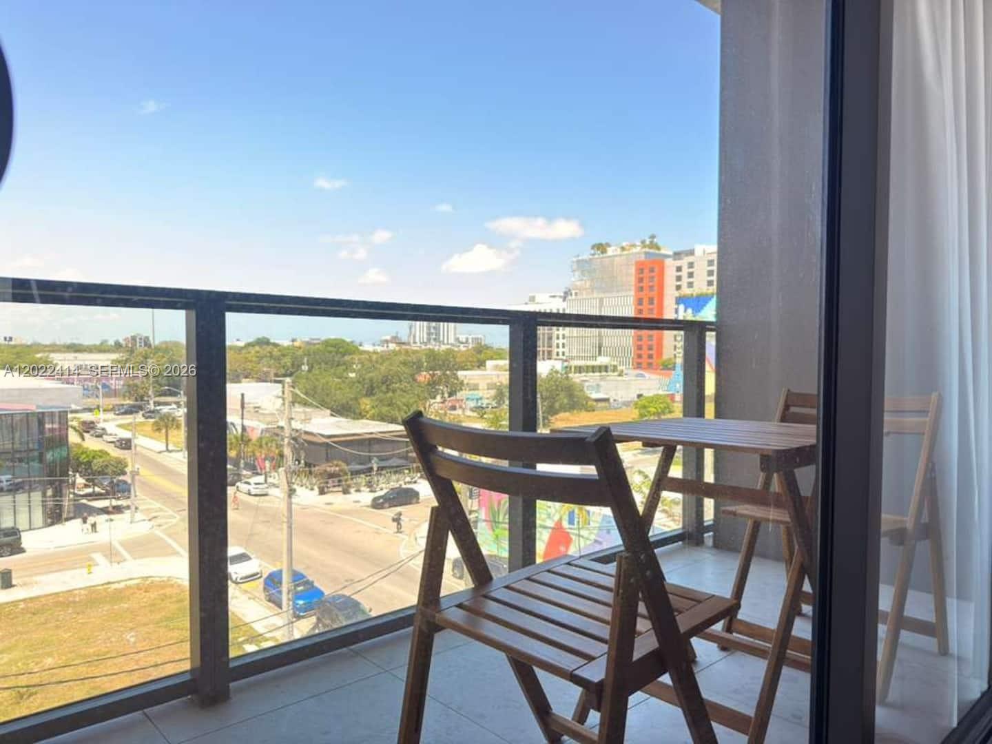 A balcony with a wooden table and chairs overlooks a city street and buildings — 2700 NW 2nd Ave # 424, Miami FL 33127, MIAMI, FL