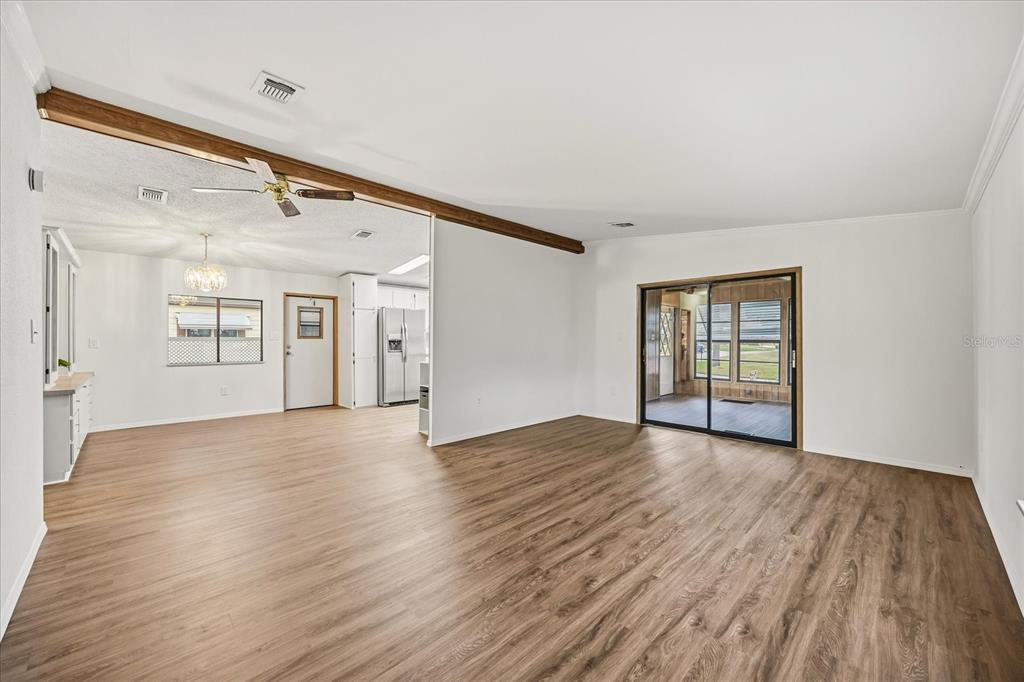A spacious living room with wood-look flooring opens into a kitchen with white cabinets — 2446 FAIRBLUFF CIRCLE UNIT 1554, ZELLWOOD, FL