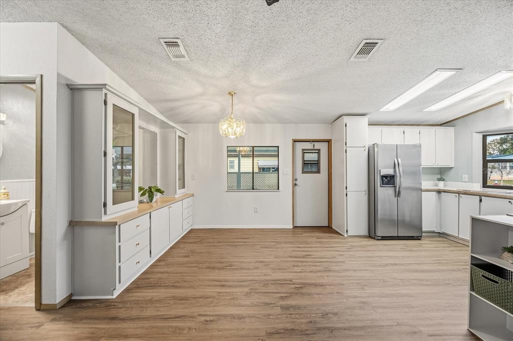 A kitchen and dining area with white cabinets, stainless steel appliances, and wood-look flooring — 2446 FAIRBLUFF CIRCLE UNIT 1554, ZELLWOOD, FL