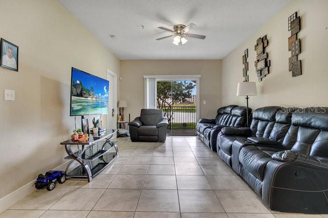 A living room features a television, a leather sofa, an armchair, and a sliding glass door — 3702 PALM DESERT LANE UNIT 5414, ORLANDO, FL