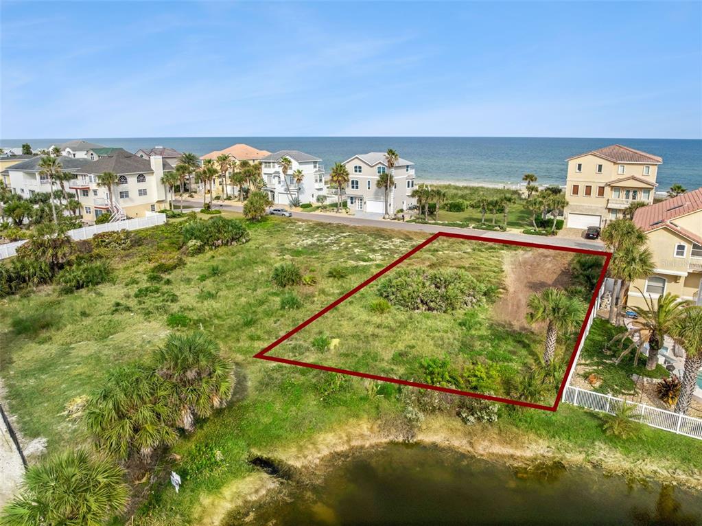 An aerial view shows a vacant, grass-covered residential lot outlined in red near the ocean — 22 OCEAN DUNE CIRCLE, PALM COAST, FL