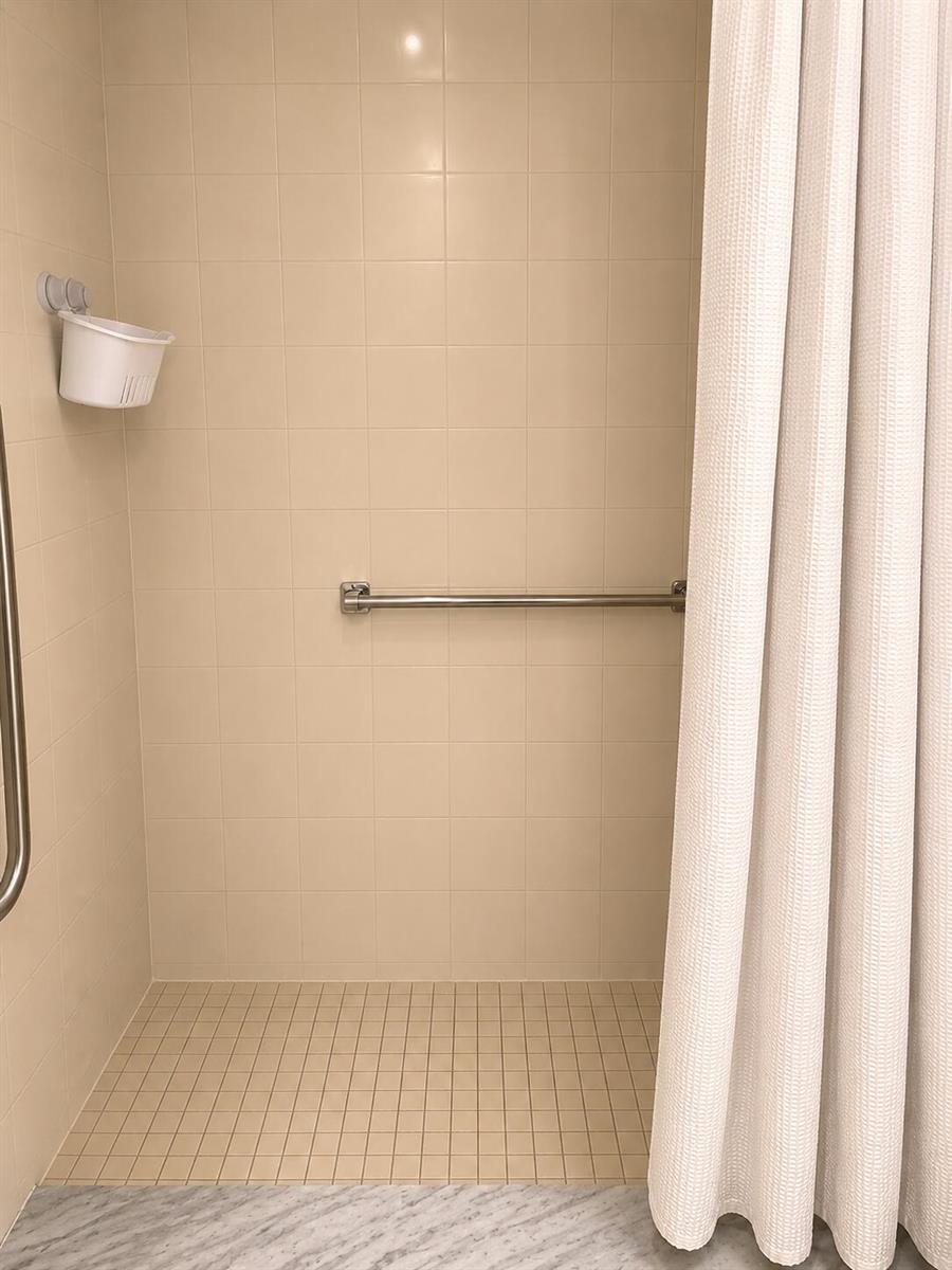 A walk-in shower with beige tiled walls, a grab bar, and a white shower curtain — 3067 Yarmouth D, Boca Raton FL 33434, BOCA RATON, FL