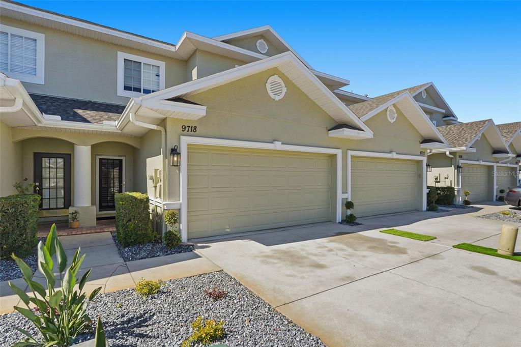 The exterior of a multi-unit townhouse features beige stucco walls, shingled roofs, and concrete driveways — 9718 TAYLOR ROSE LANE, SEMINOLE, FL