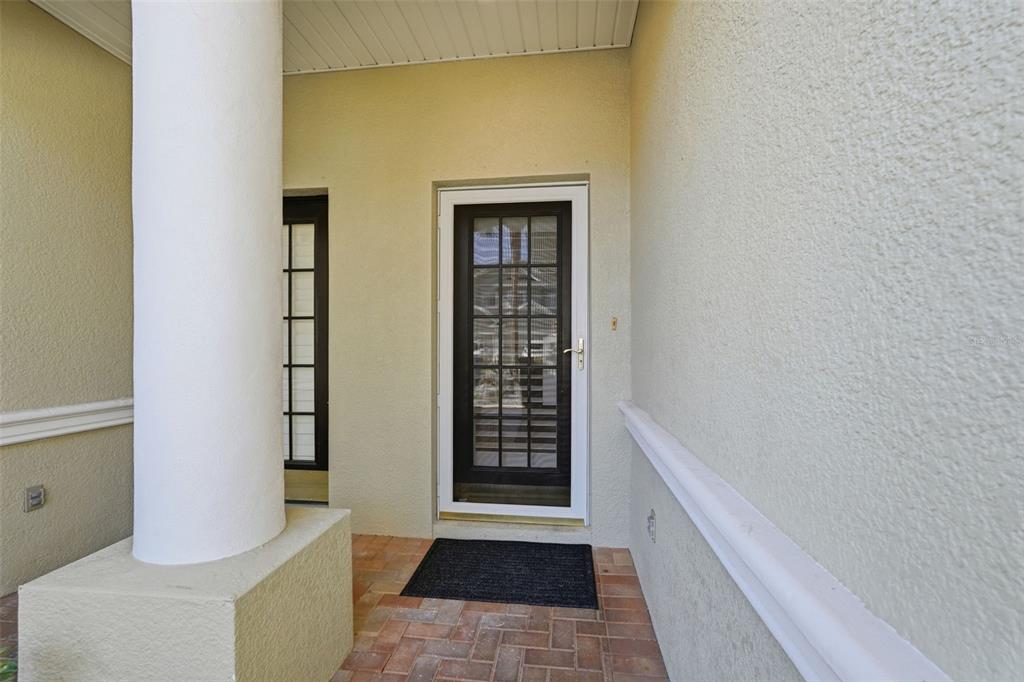 A covered entryway features a white column, a brick floor, and a glass storm door — 9718 TAYLOR ROSE LANE, SEMINOLE, FL
