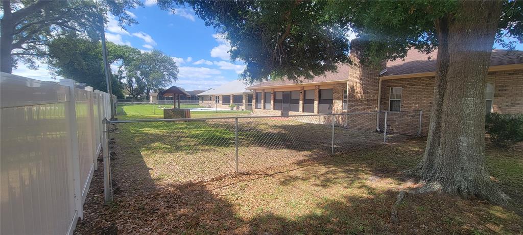 A backyard features a brick house, a chain-link fence, and a large tree — 1991 TILBURG AVENUE, DELTONA, FL
