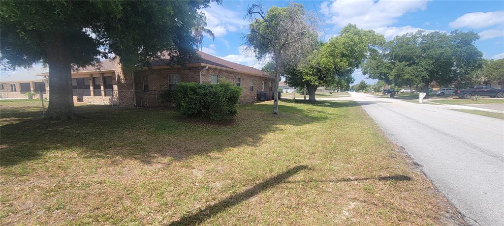 A brick house with a fenced yard and large trees sits beside a paved street — 1991 TILBURG AVENUE, DELTONA, FL