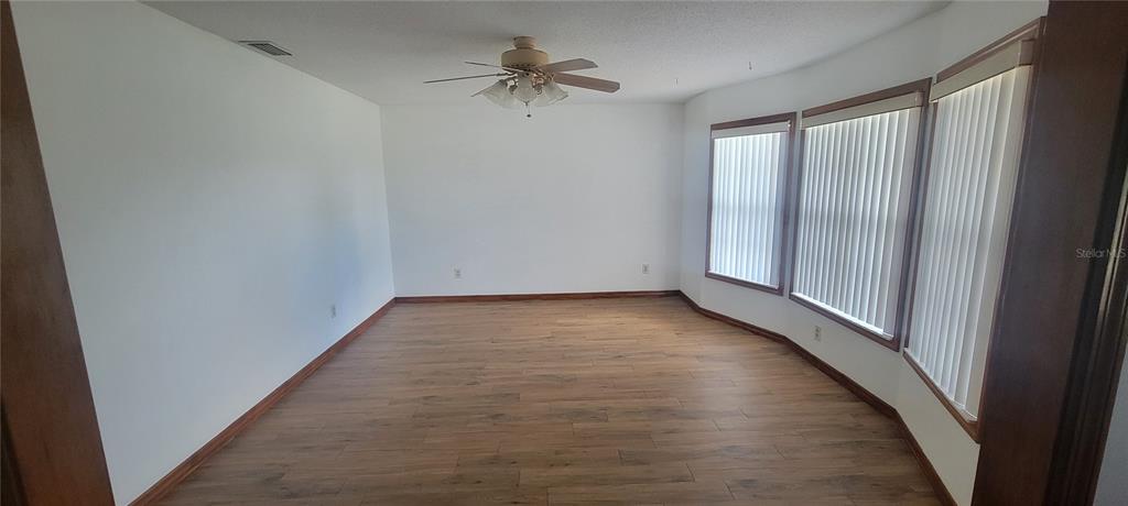An empty room features wood-look flooring, white walls, a ceiling fan, and a bay window — 1991 TILBURG AVENUE, DELTONA, FL