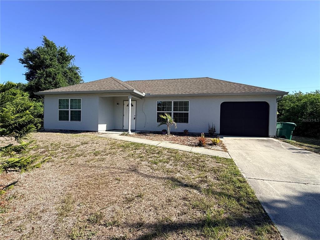 A single-story house with a light-colored exterior, a dark garage door, and a concrete driveway — 9064 BENSONHURST LANE, ENGLEWOOD, FL