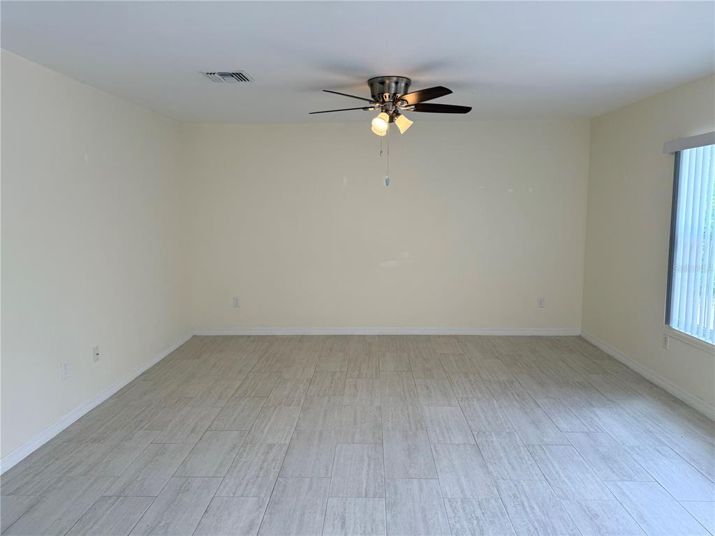 An empty room features light-colored tile flooring, cream-colored walls, and a ceiling fan — 9064 BENSONHURST LANE, ENGLEWOOD, FL