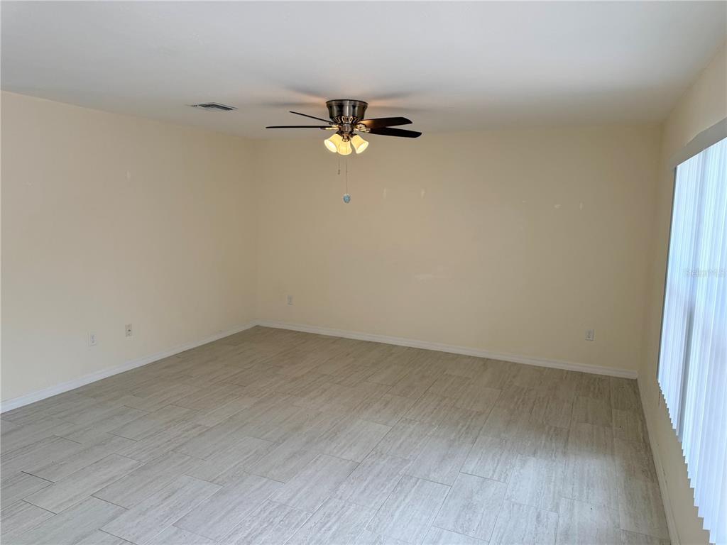 An empty room with light-colored tile flooring, beige walls, and a ceiling fan — 9064 BENSONHURST LANE, ENGLEWOOD, FL