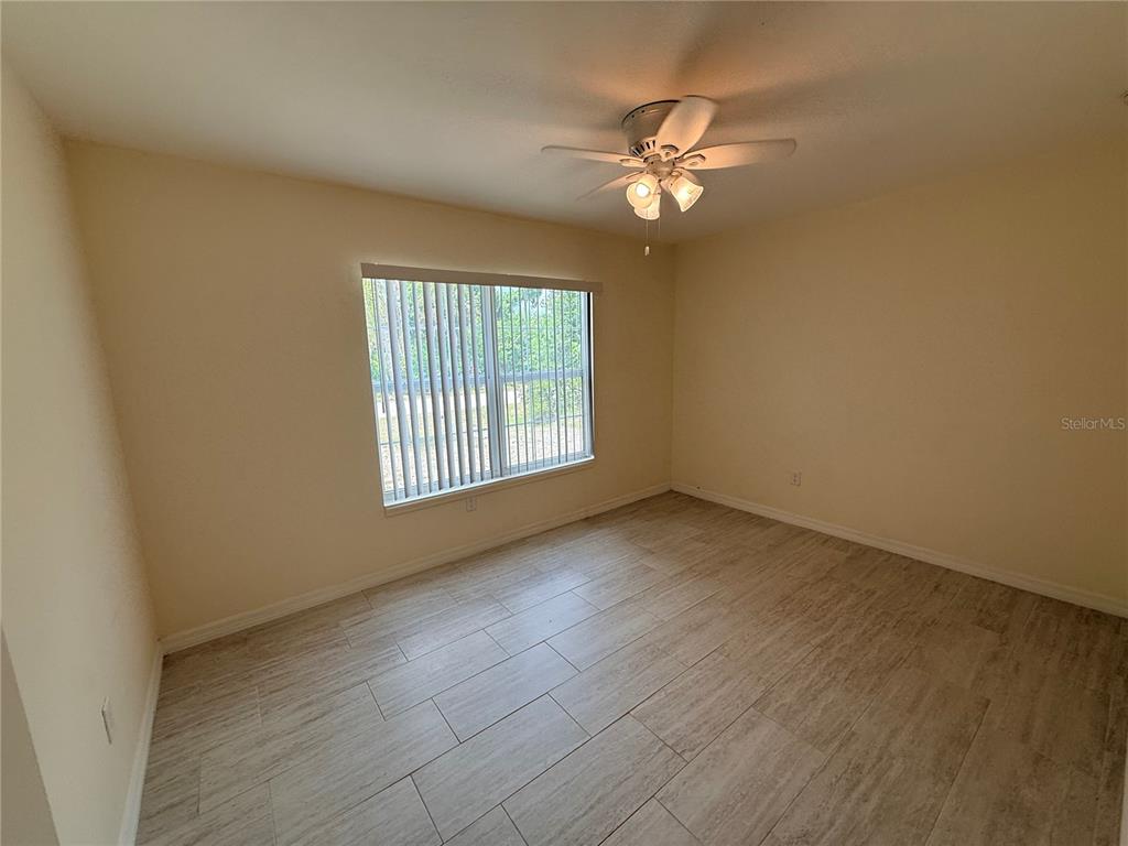 An empty bedroom features light-colored tile flooring, beige walls, and a ceiling fan — 9064 BENSONHURST LANE, ENGLEWOOD, FL