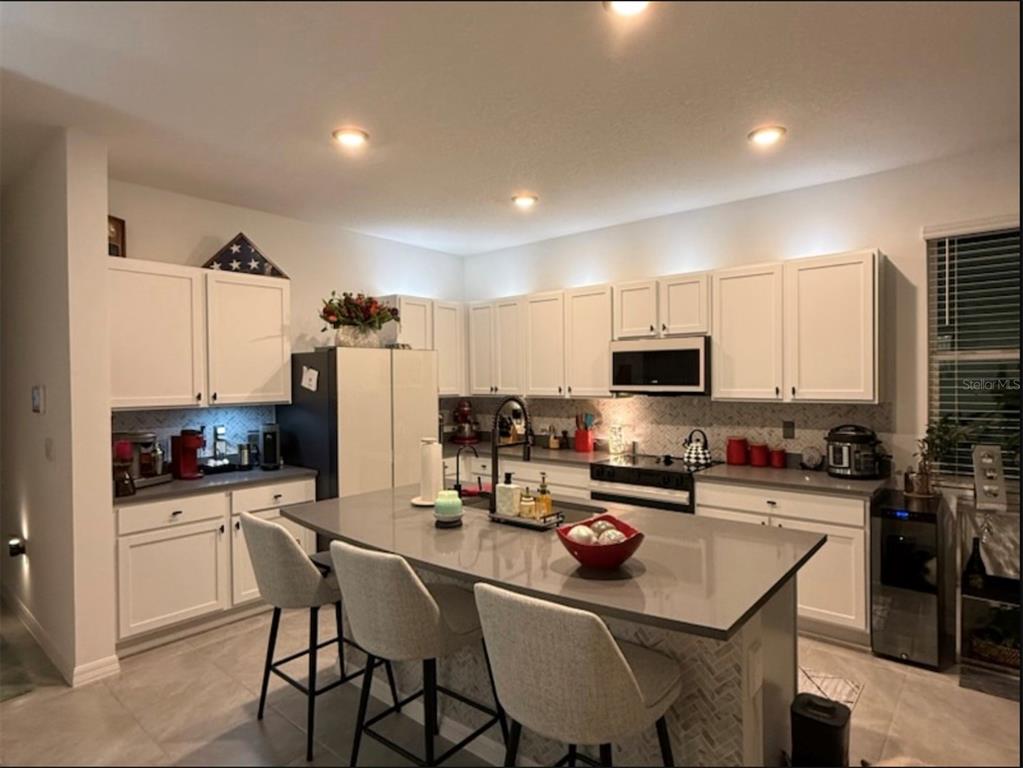 A kitchen features white cabinets, a large gray island with seating, and stainless steel appliances — 388 MANGROVE SHADE CIRCLE, APOLLO BEACH, FL