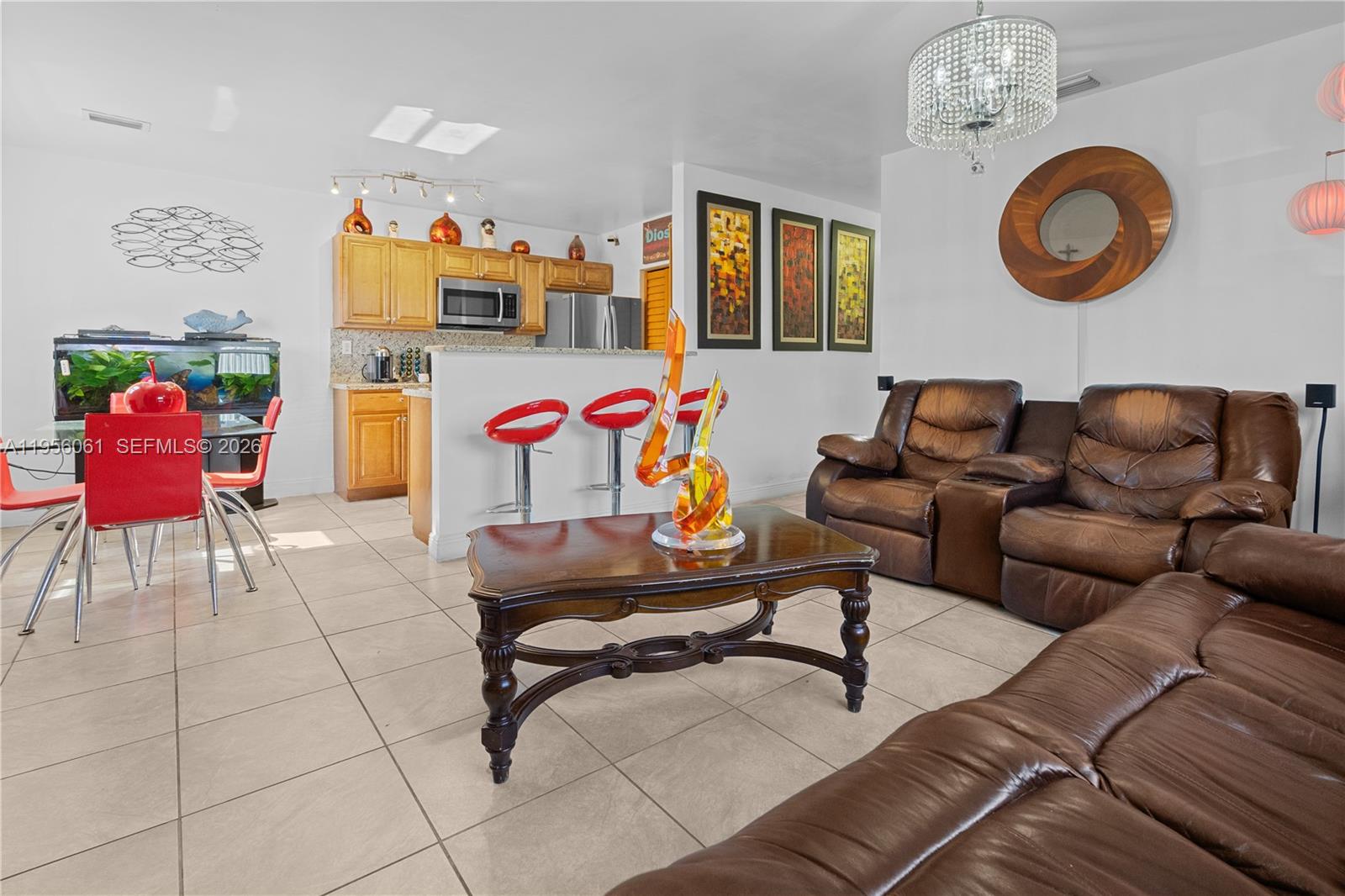 A living room and kitchen area feature tile floors, brown leather sofas, and red bar stools — 1031 NE 213th Ter, Miami FL 33179, MIAMI, FL
