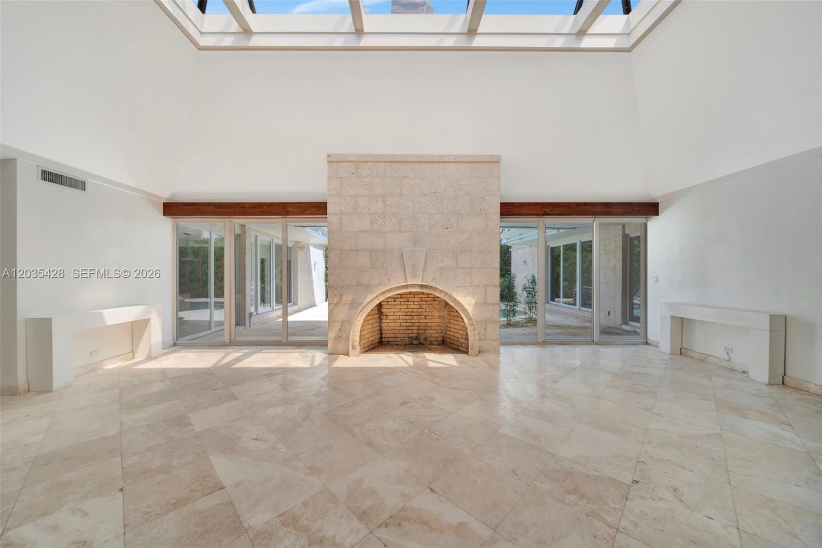 A spacious living room features a central stone fireplace, tile flooring, and a large skylight — 111 S Hibiscus Dr, Miami Beach FL 33139, MIAMI BEACH, FL