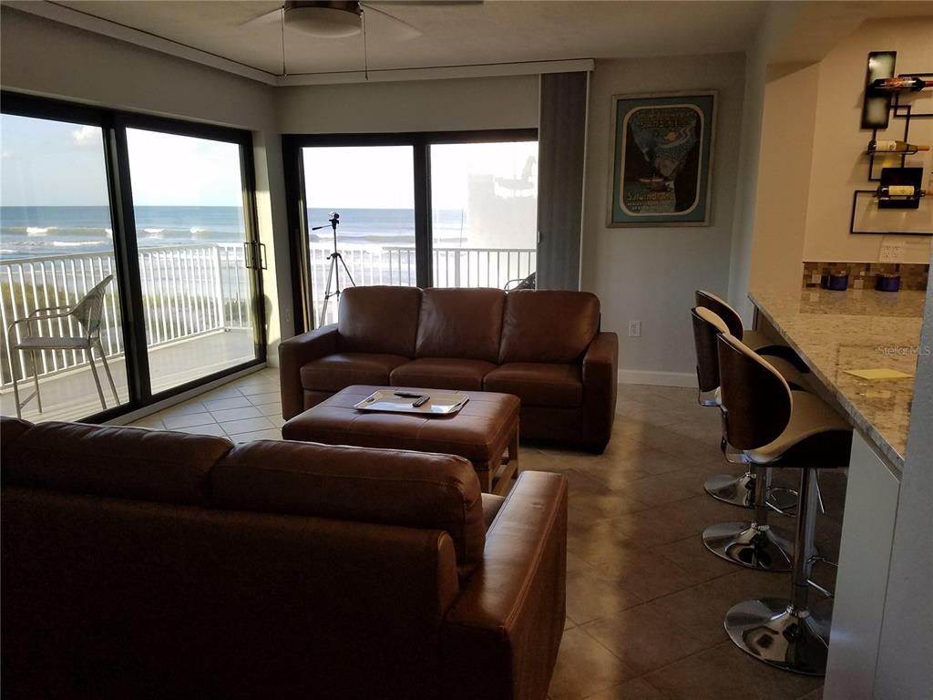 A living room with brown leather furniture overlooks the ocean through large sliding glass doors — 1571 S ATLANTIC AVENUE UNIT 211, NEW SMYRNA BEACH, FL